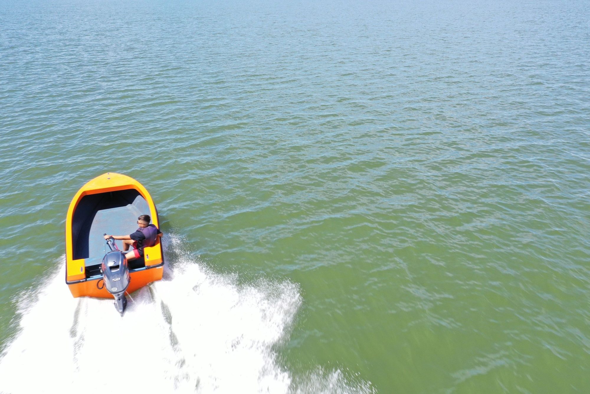 Orange and white Mighty Boy running across the lake, seen from above